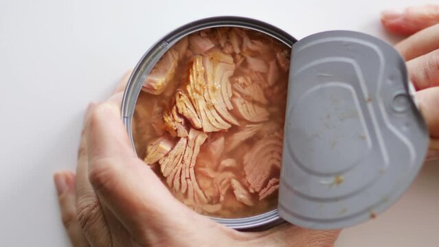 Hand open canned preserved tuna fish meat on white background. Flat lay, top view