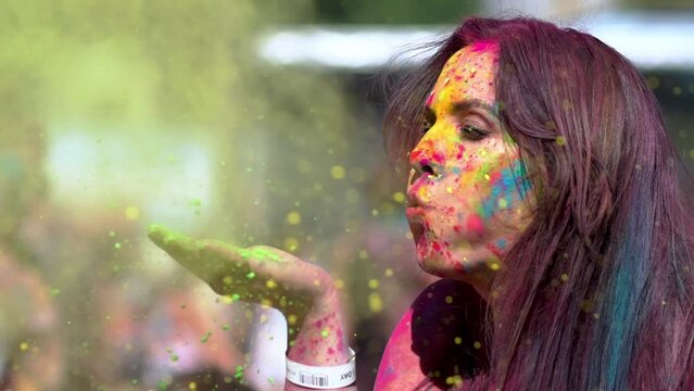Happy girl holding Holi paints in her hands and blowing them. Side view