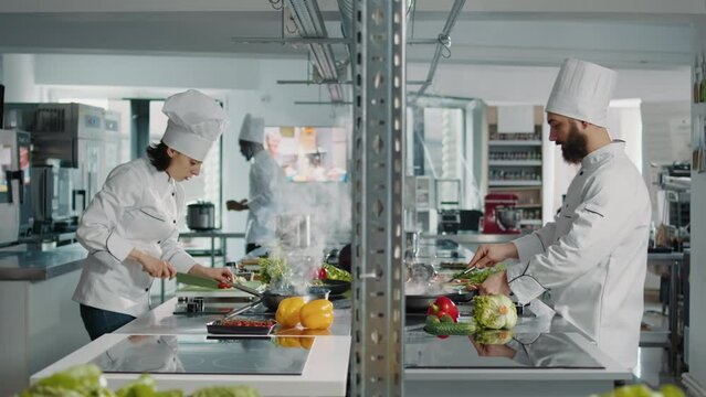 Team of cooks preparing fresh ingredients to follow culinary recipe, making gastronomic dish in authentic restaurant kitchen. People working as chefs cooking gourmet meal with vegetables.