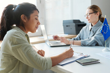 Hispanic woman applying for visa having appointment in embassy signing documents while consular...