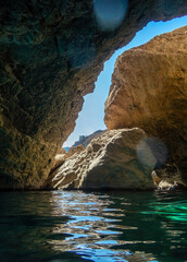 Lens flare and sea water shining under the rays of the sun inside a sea cave. Summer on a Greek island.