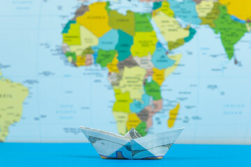 Paper ship made of dollars in front of world map, ship transportation concept, American warship and war finance idea, international trade with American dollar, paper ship on blue ground © Hakan