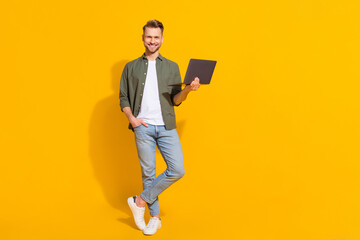 Full length body size view of attractive cheerful guy using laptop booking order isolated over bright yellow color background