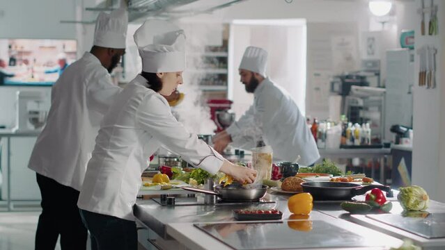 Professional chef preparing bell pepper ingredient on cutting board, adding vegetables on gourmet meal dish. Authentic woman cooking delicious food in restaurant kitchen. Handheld shot.