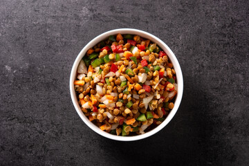 Lentil salad with peppers,onion and carrot in bowl on black background. Top view