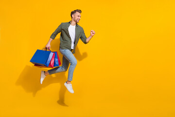 Fototapeta na wymiar Full length body size view of attractive cheerful guy jumping buying things running isolated over bright yellow color background