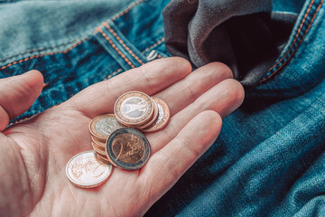 Euro coins on a male palm against the background of empty jeans pockets