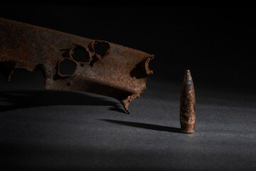 close-up of a rusty pierced metal profile and a fired bullet on a dark background