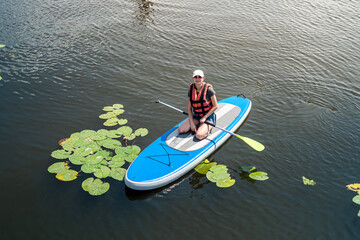 beautiful young woman in a protective vest learns to swim on a sup board on a city lake