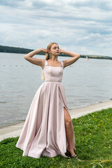 Young woman in long pink evening dress standing alone near lake at city park