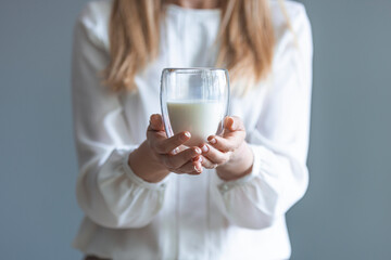 Woman hand holding glass of fresh milk on white background. Woman drinking a glass of milk in the kitchen at home. Healthy drink concept. Girl hand showing glass full of milk