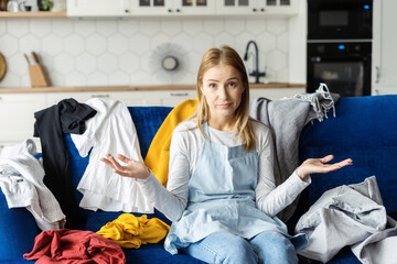 Unhappy woman in apron with bunch of colourful clothes