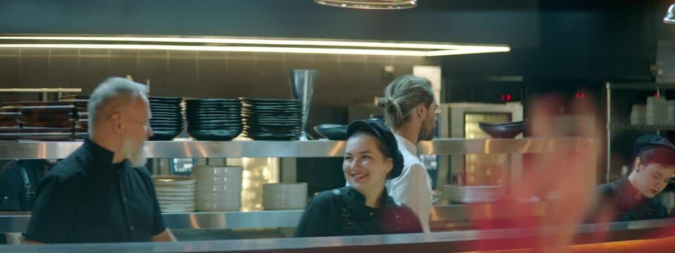 TRACKING Chef walking through busy commercial restaurant kitchen, checking new orders on a display. Shot with 2x anamorphic lens