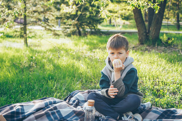 Boy 7-8 years old sitting on plaid and eating apple. Concept of spring or summer picnic
