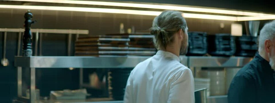 TRACKING Chef walking through busy commercial restaurant kitchen, checking new orders on a display. Shot with 2x anamorphic lens