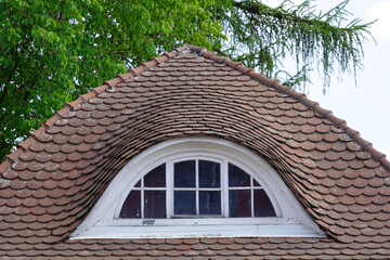 Curved tiled roof and a round dormer window with lattice windows. 