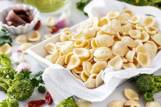 Orecchiette con cime di rapa ingredients typical of Apulia regional cuisine - homemade fresh pasta, turnip greens, chilli pepper, garlic and anchovy at the background