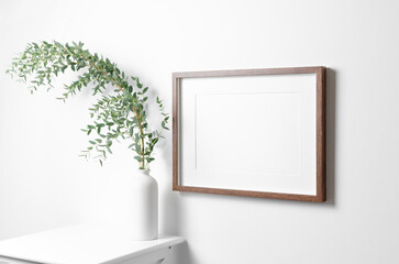 Landscape frame mockup for artwork or picture on white wall with eucalyptus twigs.