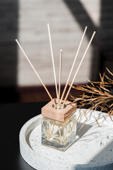 Transparent bottle of aroma diffuser on the terazzo podium on blurred room background. Eau de parfum for home presentation on a podium with field flowers. Trending concept in natural materials.