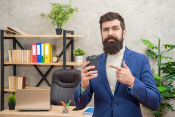 mature entrepreneur in jacket having coffee break point finger on cup at office, coffee break