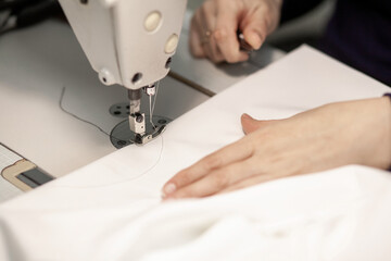 Hands of a dressmaker sewing clothes from white fabric on a sewing machine, close-up