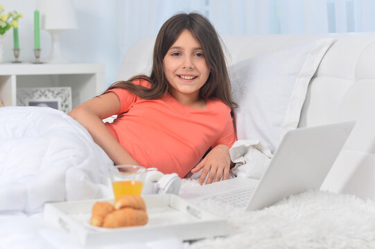 Beautiful girl  lying on soft beige bed with laptop and having breakfast