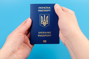 Passport of a citizen of Ukraine in a female hand on a blue background, close-up. Inscription in Ukrainian Ukraine Passport