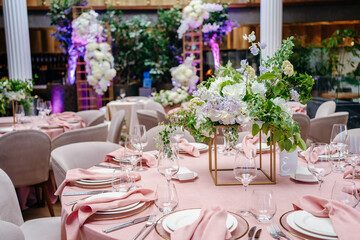 Banquet table is decorated with plates, cutlery, glasses and flower arrangements