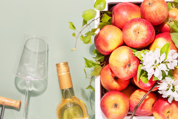 Bottle of apple wine with glass, corkscrew and farm apples in a white wooden box on a green background with copy space. Summer Refreshing Low-alcohol fruit drink. Fruit wine. Soft focus style