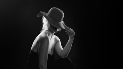 woman in a hat and black shirt on a dark background. Back light.