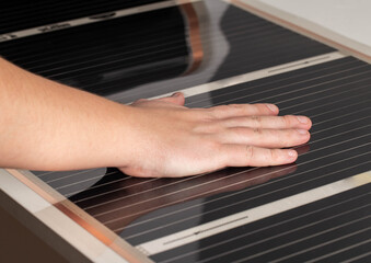 A man checks with his hand the heat from the infrared floor heating after installation. Close-up