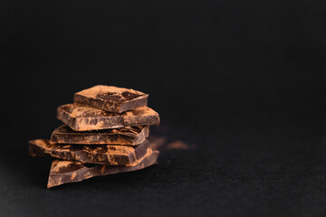 Close up view of pieces of dark chocolate with dry cocoa on black surface.