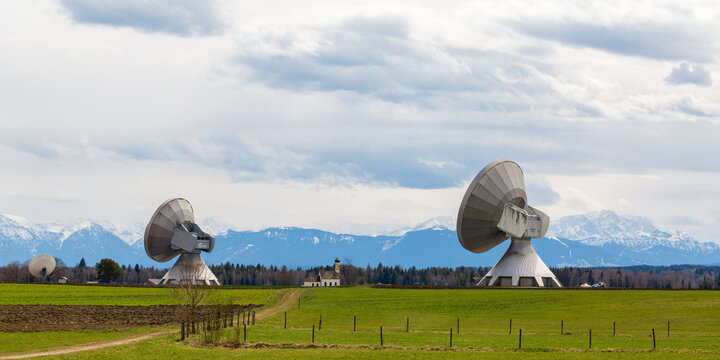 Two satellite dishes of the Raisting radome, pointing towards the sky. In the middle a church, in the background the alps.