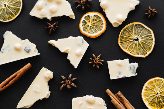 Top view of slices and dry orange slices near white chocolate on black background.