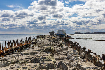 An old abandoned stone pier goes into the sea. An old ship is moored. A sunny day with clouds in Baltiysk, Kalinigrad region, Russia, near the Baltic sea.