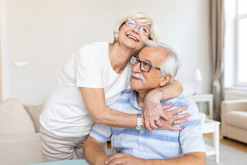 Portrait loving older wife hugging husband sitting on cozy couch. Happy senior mature couple smilling