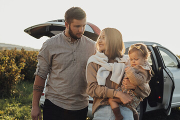 Young Caucasian Family Enjoying Road Trip, Mother and Father with Little Daughter Outdoors with SUV Car on the Background