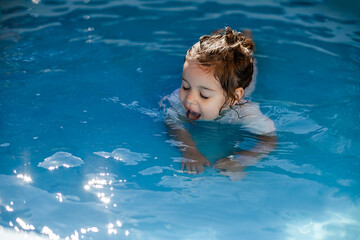A little girl is in the pool and drinks water from the pool. The concept of summer holidays and...