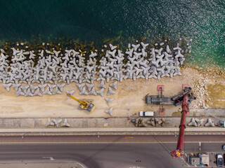 Aerial view of breakwater construction. Bulldozer and crane on a pile of boulders in the sea