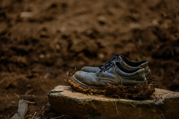 Old dirty boots on the rock, full of clay and mud at the boots.