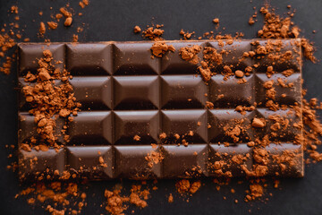 Top view of natural cocoa on chocolate bar on black background.