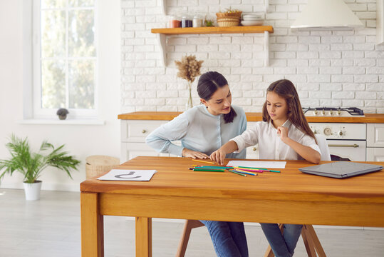 Caring mom and small teen daughter relax at home kitchen draw earn together with colorful pencils. Loving mother or nanny play paint with little girl child, engaged in art hobby activity.