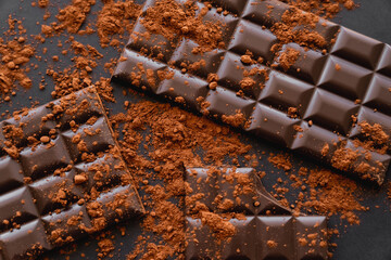 Top view of natural cocoa and chocolate bars on black background.