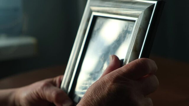 An elderly woman holds an old family photo in a frame in her hands, close-up. The concept of nostalgia, grief, longing and loneliness in old age