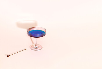 Elegant crystal Art Deco glass, blue drink, cocktail skewer. Minimal creative summer relax concept. Powdery pink background. 