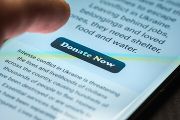 Close-up finger pressing donate icon button on smartphone screen. Donation money online concept