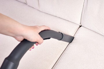 Close-up of a female hand vacuums the surface of the beige sofa - obrazy, fototapety, plakaty