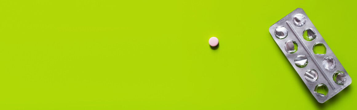 top view of used blister pack near round shape pill on green background, banner.