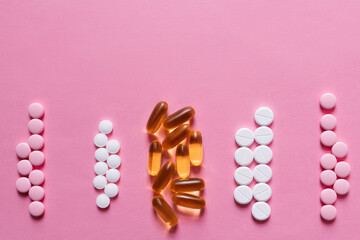 flat lay view of different round shape pills and jelly capsules on pink background.