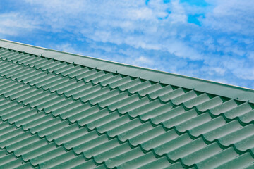 Fototapeta na wymiar A green roof made of metal in the form of tiles against a blue sky. Place for text